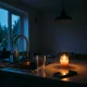A dimly lit kitchen during a power outage at dusk: a kitchen tap with a single glass beside it, a dark ceiling light, and a phone on the counter with a dead screen, while a warm ca